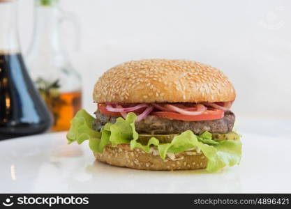 Tasty classical burger with meat cheese lettuce onion, tomato and sauce on white table