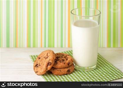 Tasty cookies and glass of milk on white wooden surface and green striped background. Dairy product concept, copy space for text. Tasty cookies and glass of milk on green background