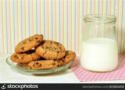 Tasty cookies and jar of milk on white wooden surface and colorful striped background. Dairy product concept, copy space for text. Tasty cookies and jar of milk on colorful striped background