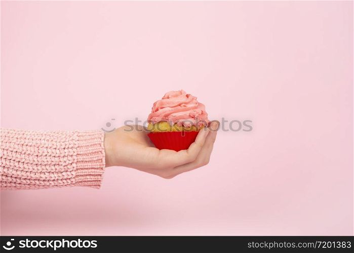 Tasty cupcake on female hand on a light pink background. Monochrome festive concept with cupcake and pink frosting. Copy space.. Monochrome festive concept with cupcake and pink frosting. Copy space.