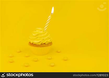 Tasty cupcake with birning candle on a yellow background. Monochrome birthday concept banner with cupcake and yellow frosting and yellow candy. Copy space.. Monochrome birthday concept banner with cupcake and yellow frosting and yellow candy