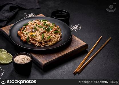 Tasty dish of Asian cuisine with rice noodles, chicken, asparagus, pepper, sesame seeds and soy sauce on dark concrete background. Tasty dish of Asian cuisine with rice noodles, chicken, asparagus, pepper, sesame seeds and soy sauce