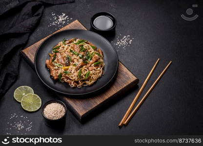 Tasty dish of Asian cuisine with rice noodles, chicken, asparagus, pepper, sesame seeds and soy sauce on dark concrete background. Tasty dish of Asian cuisine with rice noodles, chicken, asparagus, pepper, sesame seeds and soy sauce