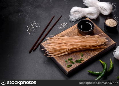 Tasty dish of Asian cuisine with rice noodles, chicken, asparagus, pepper, sesame seeds and soy sauce on dark concrete background. Tasty dish of Asian cuisine with rice noodles, chicken, asparagus, pepper, sesame seeds and soy sauce