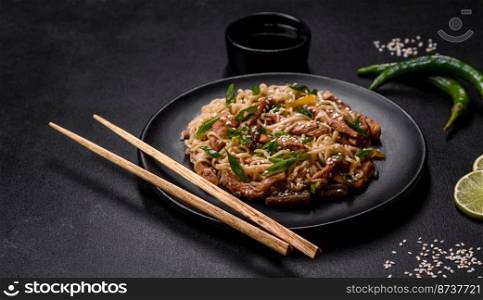 Tasty dish of Asian cuisine with rice noodles, chicken, asparagus, pepper, sesame seeds and soy sauce on dark concrete background. Tasty dish of Asian cuisine with rice noodles, chicken, asparagus, pepper, sesame seeds and soy sauce