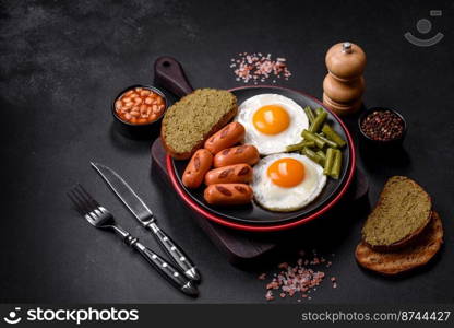 Tasty English breakfast of fried eggs, beans, asparagus, sausages with spices and herbs on a dark concrete background. Tasty English breakfast of fried eggs, beans, asparagus, sausages with spices and herbs