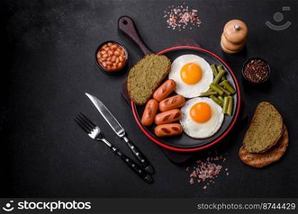 Tasty English breakfast of fried eggs, beans, asparagus, sausages with spices and herbs on a dark concrete background. Tasty English breakfast of fried eggs, beans, asparagus, sausages with spices and herbs