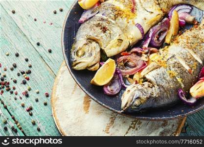 Tasty fish fried in onion and lemon. Baked rainbow trout, seafood. Whole roasted trout.