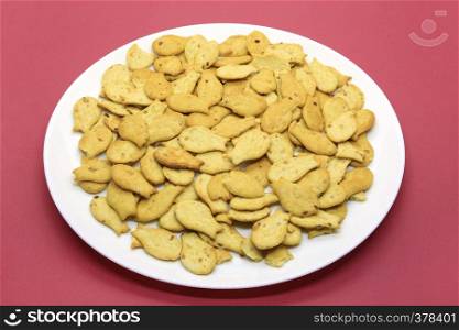 Tasty fish-shaped cookies in a white plate closeup on a crimson background