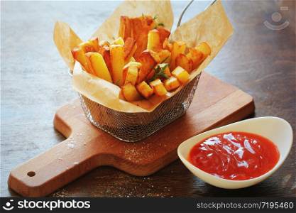 Tasty french fries and potato chips in metal baskets on wooden table, on darkt background .. Tasty french fries and potato chips in metal baskets on wooden table, on darkt background