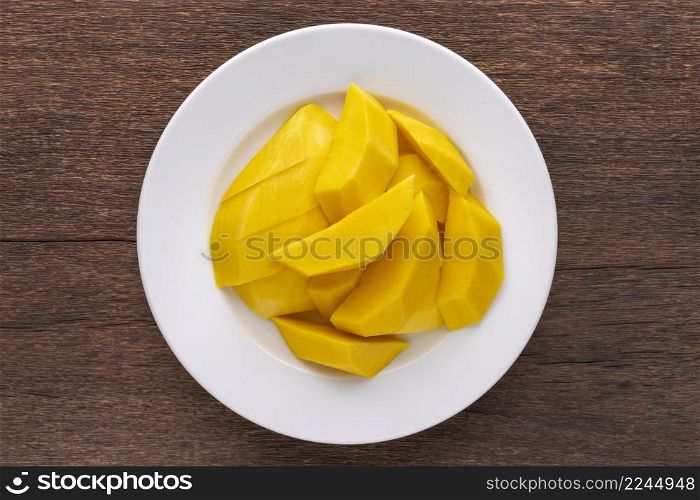 tasty fresh yellow ripe mango in simply white ceramic plate on rustic natural wood texture background, top view