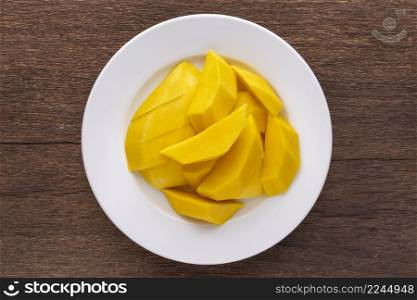 tasty fresh yellow ripe mango in simply white ceramic plate on rustic natural wood texture background, top view