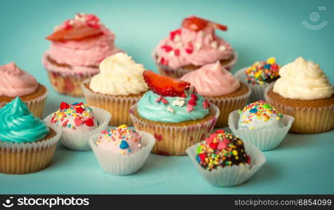 Tasty freshly baked cupcakes and colorful candies over turquoise background