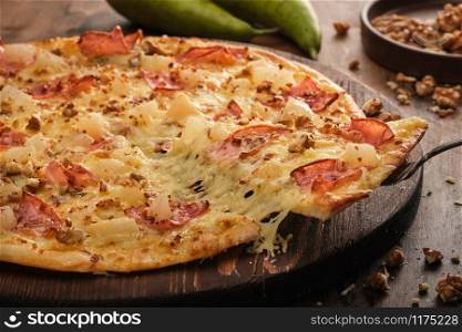 Tasty freshly prepared pizza with pear, nuts and bacon on a wooden board, rustic style.