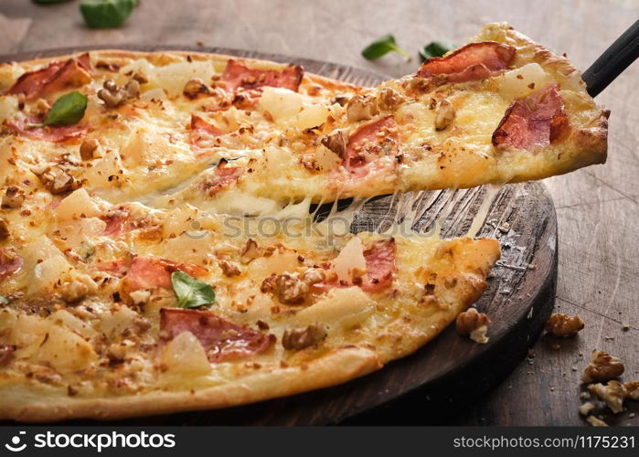 Tasty freshly prepared pizza with pear, nuts and bacon on a wooden board, rustic style.