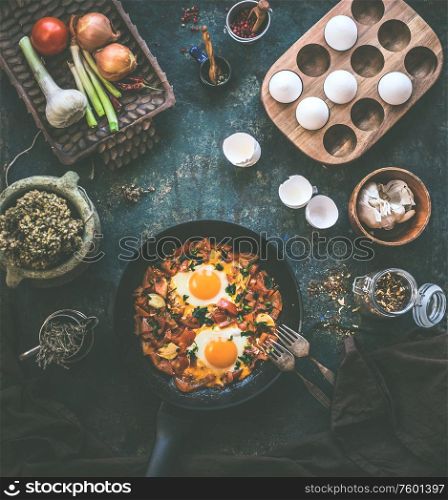 Tasty fried eggs in tomato sauce in black pan with fork on rustic background. Top view. Shakshuka breakfast. Ingredients. Cooking. Healthy food eating