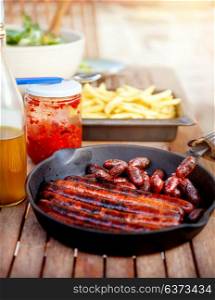 Tasty fried pork sausages from the grill, french fries and sauce on the table, barbecue picnic outdoors, delicious unhealthy food
