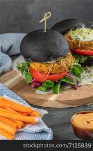 Tasty grilled veggie burger with chickpeas and vegetables on black bread on wooden background