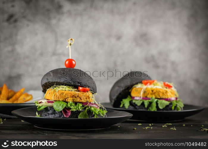 Tasty grilled veggie burgers with chickpeas and vegetables on black bread on dark wooden countertop.