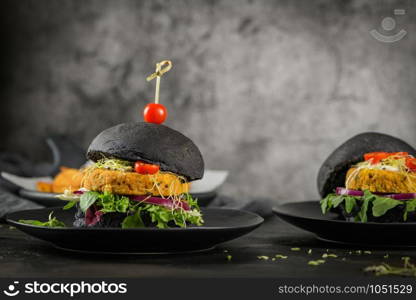 Tasty grilled veggie burgers with chickpeas and vegetables on black bread on dark wooden countertop.