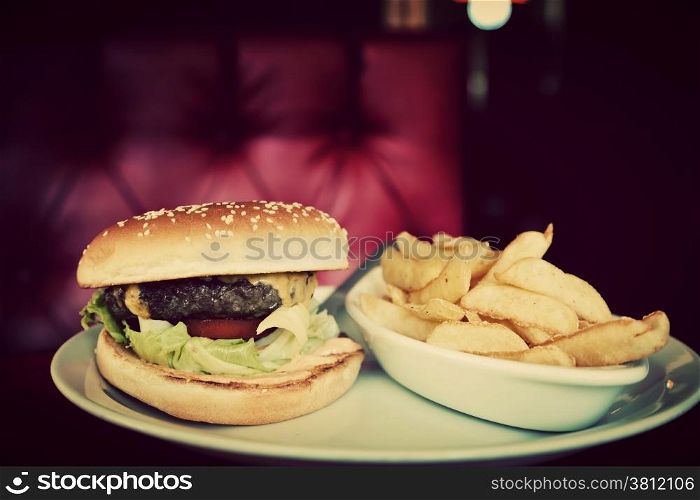 Tasty hamburger and french fries on plate in american food restaurant. Red leather sofa in the background. Vintage, retro style