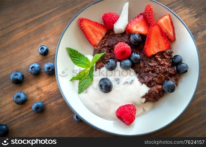 Tasty healthy breakfast, fresh juicy fruits and berries on the plate with yogurt and granola, beautiful food still life on the wooden table background, delicious vegetarian food