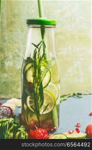 Tasty infused water in bottle with drink straw and ingredients, front view. Water Flavored with green fruits, cucumber and herbs. Summer drinks. Healthy and clean detox beverages.