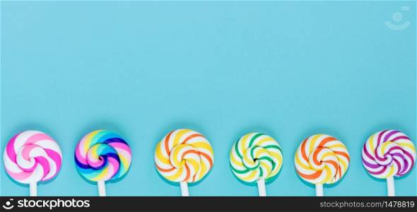 Tasty lollipops on blue pastel paper color background, Set of realistic spiral striped colorful lollipops on white plastic sticks, Summer and pop art concept. Top view.