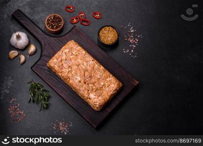 Tasty meat brawn or roll on a wooden cutting board with spices and herbs on a dark concrete background. Tasty meat brawn or roll on a wooden cutting board with spices and herbs