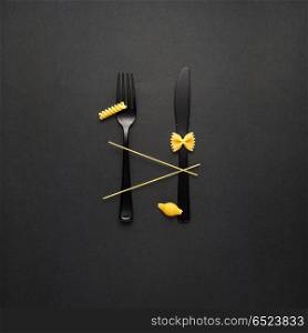 Tasty pasta.. Creative still life photo of fork and spoon with raw pasta on black background.