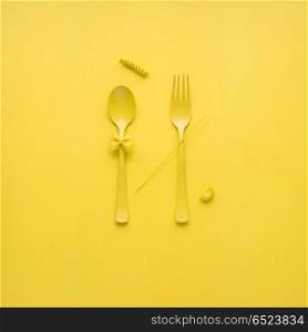 Tasty pasta.. Creative still life photo of fork and spoon with raw pasta on yellow background.