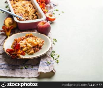 Tasty peach crumble dessert in plate on light background with baking pan and fresh peaches . Copy space