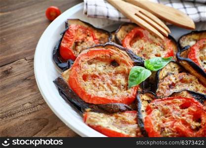 Tasty pizza topping, roasted aubergine with tomatoes and basil on the plate on the wooden table, delicious homemade food