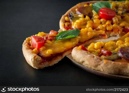 Tasty pizza with cherry tomatoes and sliced slice on a black background. Delicious italian pizza with cheese and cherry tomatoes on a round board, sliced triangular piece. Authentic national dish of Mediterranean cuisine.. Tasty pizza with cherry tomatoes and sliced slice on a black background.