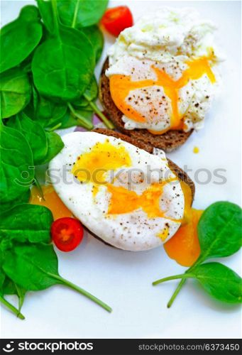 Tasty poached eggs on the bread with fresh green baby spinach and cherry tomatoes on the white plate, healthy dietary breakfast, delicious organic nutrition