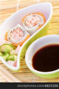 Tasty prepared sushi with avocado, cucumber, crab and salmon, eating by wooden chopsticks, served with soy sauce and ginger, healthy food
