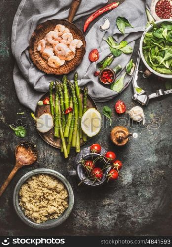 Tasty quinoa salad preparation with wooden spoon , Shrimps , asparagus and various healthy vegetables on rustic kitchen table background, top view