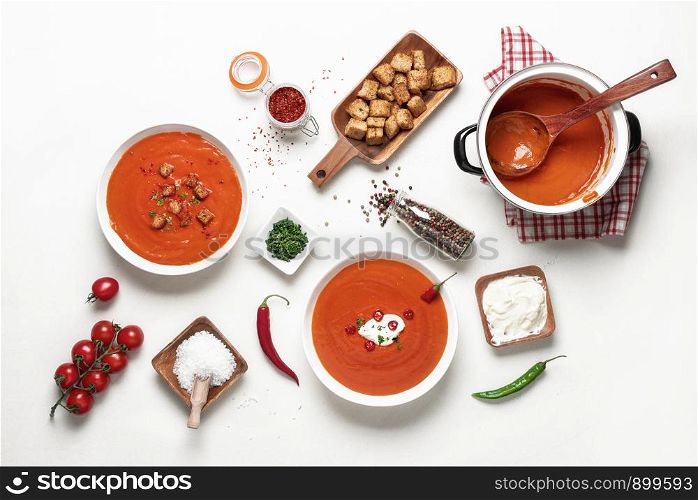Tasty red cream soup with tomatoes, chili and croutons. Above view of family dinner table. Flat lay of vegetarian meal. Tomato soup on white tabletop
