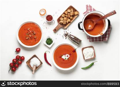 Tasty red cream soup with tomatoes, chili and croutons. Above view of family dinner table. Flat lay of vegetarian meal. Tomato soup on white tabletop
