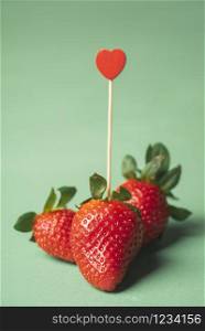 Tasty ripe strawberries with a heart-shaped toothpick on a green background. Valentine day concept. Love of strawberries. Cute Sweet summer fruits.