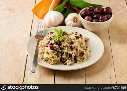 tasty risotto with black olives on wooden table with napkin and garlic