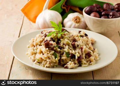 tasty risotto with black olives on wooden table with napkin and garlic