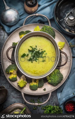 Tasty romanesco and broccoli soup in cooking pot on dark rustic background with kitchen tools, top view. Healthy and vegetarian food or diet nutrition concept.
