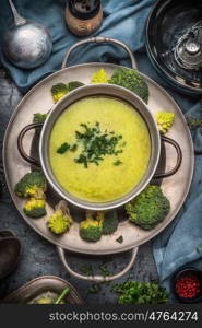 Tasty romanesco and broccoli soup in cooking pot on dark rustic background with kitchen tools, top view. Healthy and vegetarian food or diet nutrition concept.