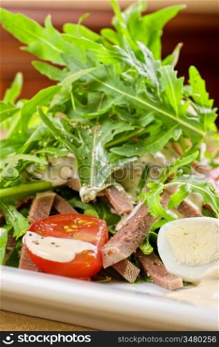 Tasty salad of beef tongue with eggs, arugula, tomato, spices and sauce