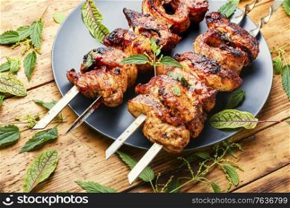 Tasty shashlik on skewers with nettle marinade.Shish kebab on wooden background. Kebabs,grilled meat with nettles