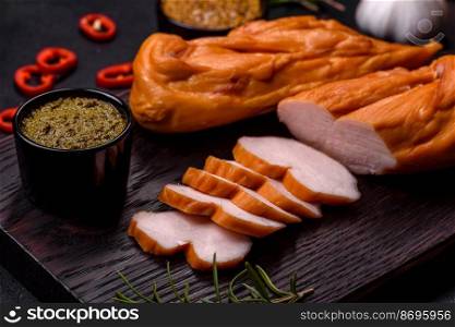 Tasty smoked fillet of chicken breast with spices and herbs on a wooden cutting board on a dark concrete background. Tasty smoked fillet of chicken breast with spices and herbs on a wooden cutting board