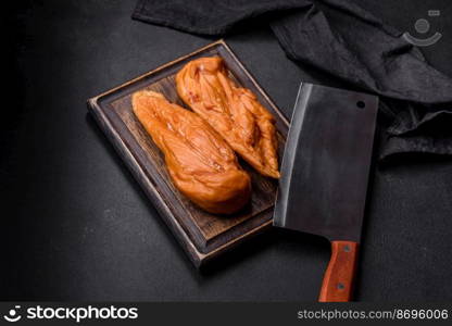 Tasty smoked fillet of chicken breast with spices and herbs on a wooden cutting board on a dark concrete background. Tasty smoked fillet of chicken breast with spices and herbs on a wooden cutting board