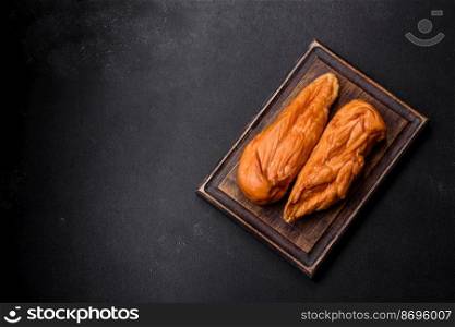 Tasty smoked fillet of chicken breast with spices and herbs on a wooden cutting board on a dark concrete background. Tasty smoked fillet of chicken breast with spices and herbs on a wooden cutting board