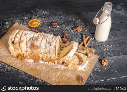 Tasty snack with homemade pound cake, filled with poppy seeds and nuts, on a baking paper and a bottle of fresh milk, on a rustic wooden table.